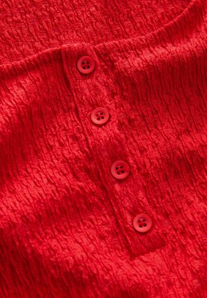 Tissu rouge texturé avec un motif froissé, présentant quatre boutons ronds de couleur rouge similaire. Vue en gros plan mettant en avant les détails.