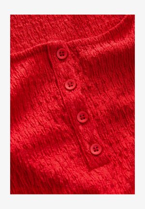 Punane tekstureeritud kangas kortsufääriga disainiga, millel on neli ümmargust nööpi sarnases punases värvuses. Suur lähedalevaade, mis toob esile detailid.