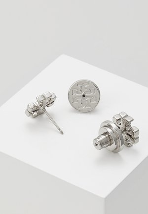 Zilverkleurige metalen studs met een symmetrisch kruisachtig ontwerp op een witte ondergrond, met voor-, zij- en achteraanzichten.