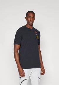 Crna majica s kratkim rukavima izrađena od pamuka. Sadrži akcentne logoe u crvenoj, bijeloj i žutoj boji na prsima. Jednostavan, klasičan kroj.