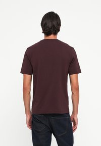Bordeauxkleurig T-shirt met korte mouwen van katoen, met een ronde hals en een relaxte pasvorm, gecombineerd met donkerblauwe denim jeans.