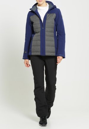 Veste isolante bleu marine et grise avec fermeture éclair à l'avant, motif de coutures verticales et capuche attachée ; associée à un pantalon noir et des chaussures noires.
