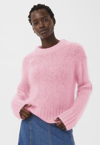 Pull rose en matière tricotée douce et duveteuse. Présente un col rond côtelé et des manches oversize avec une coupe décontractée.