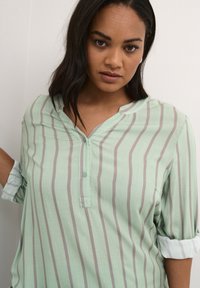 Mint green blouse with vertical gray stripes, featuring a partial button placket, roll-up sleeves, and a soft, smooth texture.