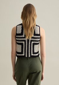 Top in bianco e nero all'uncinetto con motivi geometrici, design senza maniche e taglio corto, abbinato a pantaloni verde oliva.