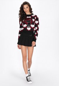 Schwarzer plissierter Rock kombiniert mit einem roten Strickpullover, der ein Katzenmotiv und Herzenmuster zeigt. Der Pullover hat lange Ärmel und einen runden Hals.