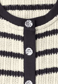 Vêtement en maille à rayures noires et blanches avec bordure noire et trois boutons métalliques brillants et texturés sur le devant.