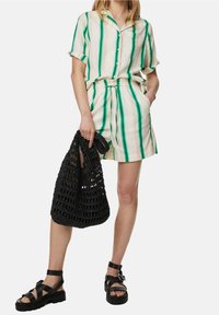 Gestreiftes kurzärmliges Hemd in Grün und Creme, kombiniert mit passenden hochgeschnittenen Shorts. Schwarze geflochtene Tasche und klobige schwarze Sandalen.