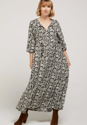 Robe maxi noire avec motif floral blanc, décolleté en V, manches trois-quarts et coupe loose, fabriquée en tissu léger. Bottes à talons brunes.
