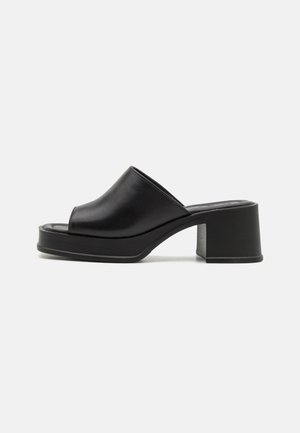 Mules à plateforme en cuir noir avec un bout ouvert rond, un petit talon carré et une texture lisse. Design minimaliste avec des lignes épurées.
