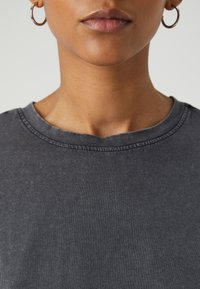 Dunkelgraues Baumwoll-T-Shirt mit Rundhalsausschnitt, kurzen Ärmeln und weicher Textur, das sichtbare Nähte entlang des Kragens zeigt.