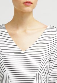 Vit topp med svarta horisontella ränder, V-ringning, mjukt material och sned sydd detalj fram.