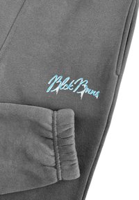 Grijze sweatpants met een gathered cuff en lichtblauwe borduurtekst "BlkBrns" nabij de zak. Zachte textuur, casual pasvorm.