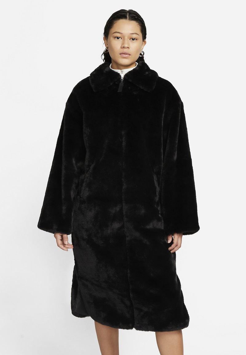 Abrigo de piel sintética negra con cuello, diseño oversized y mangas amplias, que presenta un cierre frontal y un acabado suave y texturizado.
