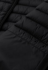 Chaleco acolchado negro con secciones de acolchado paralelo, textura suave y cremallera en la parte delantera, que ofrece un diseño elegante y funcional.