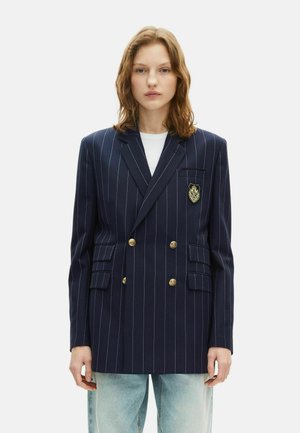 Blazer blu navy a righe con design doppiopetto, bottoni dorati e una toppa ricamata sulla tasca sinistra del petto.