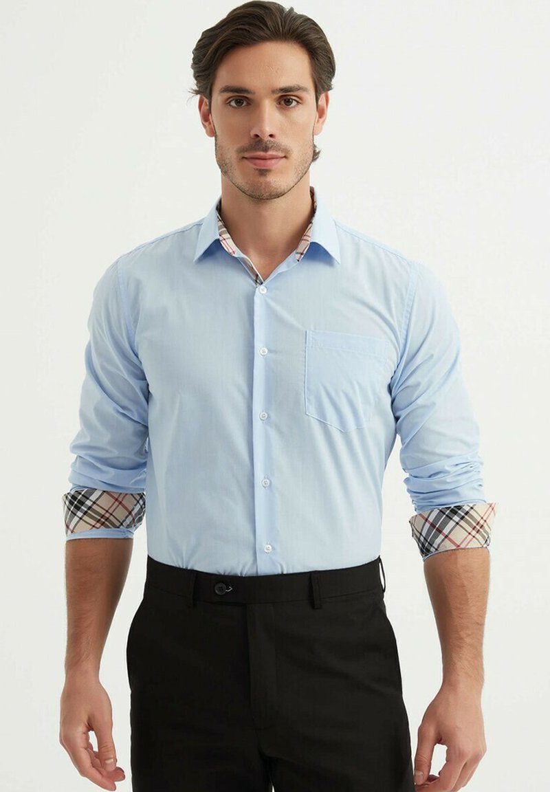 Chemise bleu clair à design boutonné, à manches longues, avec des accents à carreaux sur les poignets et le col. Comprend une poche poitrine.