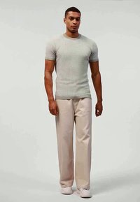 Hellgraues, strukturiertes Strick-T-Shirt mit kurzen Ärmeln, kombiniert mit cremefarbenen, locker sitzenden Hosen und weißen Sneakers.
