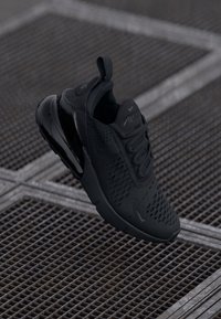 Schwarzer Nike Air Max Sneaker mit Mesh-Obermaterial und sichtbar gepolsterter Sohle, schräg auf einem Metallgitter-Oberflächenhintergrund.