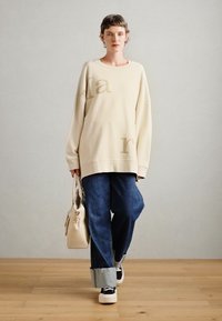 Crème sweatshirt met een oversized pasvorm en lichtbruine opdruk, gecombineerd met donkerblauwe wijde jeans en zwarte platform schoenen.