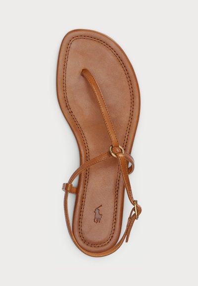 Sandália de pele castanha com sola plana, tiras finas e um detalhe em ouro circular. Costura notável ao longo das bordas e logótipo estampado no interior.
