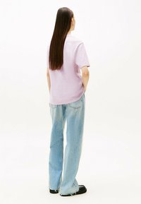 Camisa rosa de manga corta combinada con jeans holgados de color azul claro. Los jeans tienen dobladillos deshilachados y el modelo está de pie con las manos en los bolsillos.