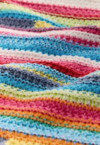 Gros plan d’un tissu tricoté multicolore avec des rayures texturées en fil bleu, rose, rouge, blanc, jaune, vert, orange et gris.