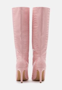 Bottes en cuir roses à motif crocodile, hautes, avec des talons pointus, montrées de l'arrière sur un fond blanc.