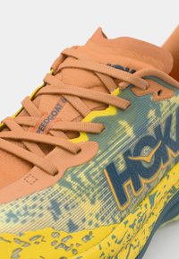 Zapatilla de trail running con parte superior de malla en naranja y azul, con detalles en amarillo, texturizados y con la marca "SPEEDGOAT 6".