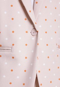 Ljusrosa kavaj med orange och vita prickar, med en enkel knappstängning och små sidofickor. Tyget har en slät textur.