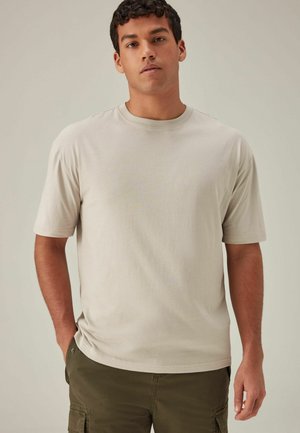 Camiseta de algodón beige con escote redondo y mangas cortas, con un corte relajado y textura suave, combinada con pantalones cortos verde oliva.