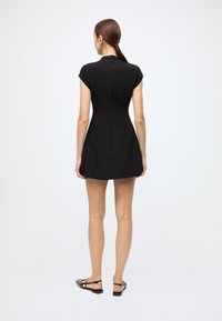 Black fitted dress with short cap sleeves, a high neckline, and a concealed back zipper. Smooth texture and above-the-knee length.