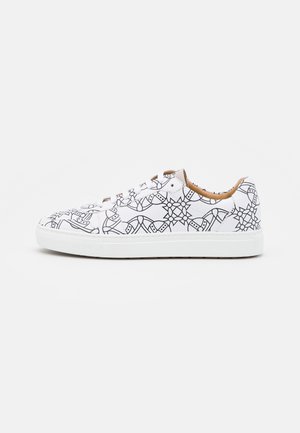 Zapatilla blanca de caña baja con patrones geométricos en líneas negras y cordones blancos sobre un fondo blanco liso.