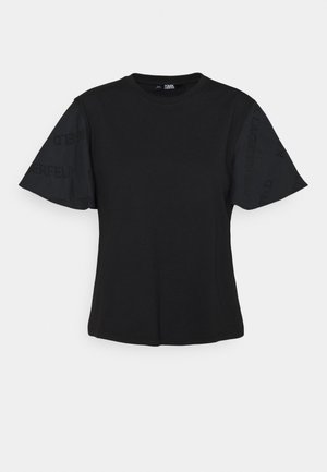 Camiseta negra de manga corta con un detalle de tela translúcida. El cuerpo principal es sólido, con un sutil logotipo en las mangas.