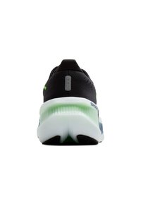 Melnas sporta apavas ar teksturētu virspusi, zaļu akcentu un mīksto balto zoli. Aizmugurējais skats izceļ papēža formu un zīmola logo.