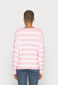 Pull rayé rose et blanc, coupe ample, texture côtelée, encolure large et manches longues. Porté avec un jean bleu.