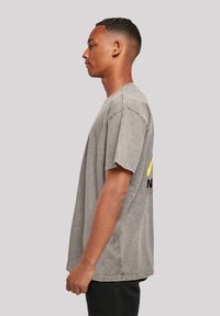 Graues kurzärmeliges T-Shirt aus verblasstem Stoff mit lockerem Schnitt. Verfügt über ein farbenfrohes Logo auf der Rückseite und einen Rundhalsausschnitt.