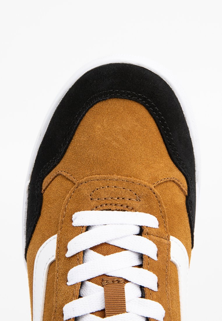 Parte superior de ante marrón con acentos negros, cordones blancos y una franja lateral blanca. Punta suave y material texturizado. Diseño de zapato deportivo.