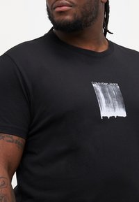 Čierne bavlnené tričko s krátkym rukávom, na prednej strane so vzorom bieleho grafického tlače "Calvin Klein Jeans" a dizajnom štetca.