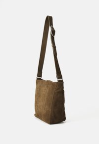 Bolso de hombro de ante marrón con forma plana, correa ajustable y herrajes plateados. Textura suave con detalles de costura visibles.