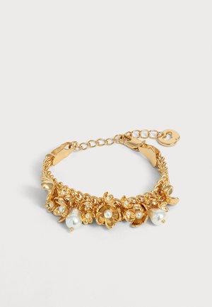 Bracelet chaîne en or avec breloques florales et accents de perles blanches, avec un petit charm en forme de cœur sur le fermoir réglable.