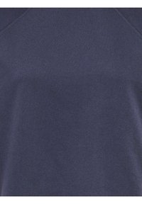 Gros plan sur un tissu bleu foncé montrant une texture douce et lisse avec des coutures visibles le long des bords supérieurs.