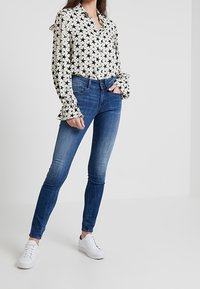 Vit blus med svart stjärntryck, med volangärmar. Tillsammans med åtsittande blå denimjeans och vita sneakers.