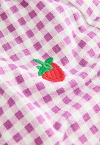 Roze en witte vichy stof met een geborduurde aardbei met groene bladeren, die een zachte textuur en een patroonontwerp laat zien.