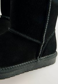 Schwarzer Wildlederstiefel mit strukturiertem Finish, sichtbaren Nähten und einer Gummisohle mit geriffeltem Muster für besseren Halt.