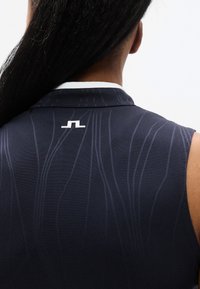 Αμάνικο πόλο μπλουζάκι σε σκουρό μπλε ύφασμα με διακριτικές ριγές υφής. Διαθέτει λευκό γιακά και λογότυπο στο πίσω μέρος.