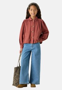 Veste boutonnée couleur rouille avec des manches bouffantes, associée à un jean bleu à jambe large et un sac fourre-tout en léopard. Bottines en suede marron.