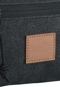 Black textured fabric pouch with a stitched brown leather label embossed with "JOHNNY URBAN" and a drawstring closure. Lightweight design.