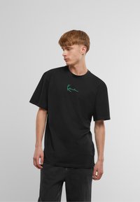 T-shirt in cotone nero con maniche corte, caratterizzato da un design ricamato verde sul petto. Vestibilità ampia con scollatura rotonda.