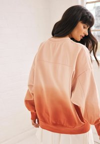 Przesadny sweter z gradientowym kolorem od jasnego brzoskwiniowego do ciemnego pomarańczowego. Miękka tkanina, szerokie rękawy oraz ściągacze przy rękawach i u dołu.